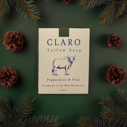 Claro Tallow Soap box labeled 'Peppermint & Pine,' surrounded by pine branches and pinecones on a green background